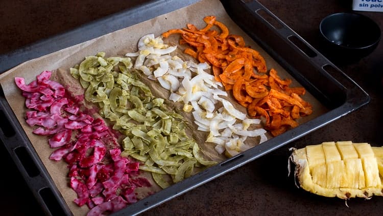 4 types of seasoned coconut chips on a baking sheet, ready for drying.