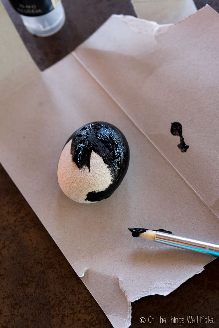 Painting a smooth, oval stone black.
