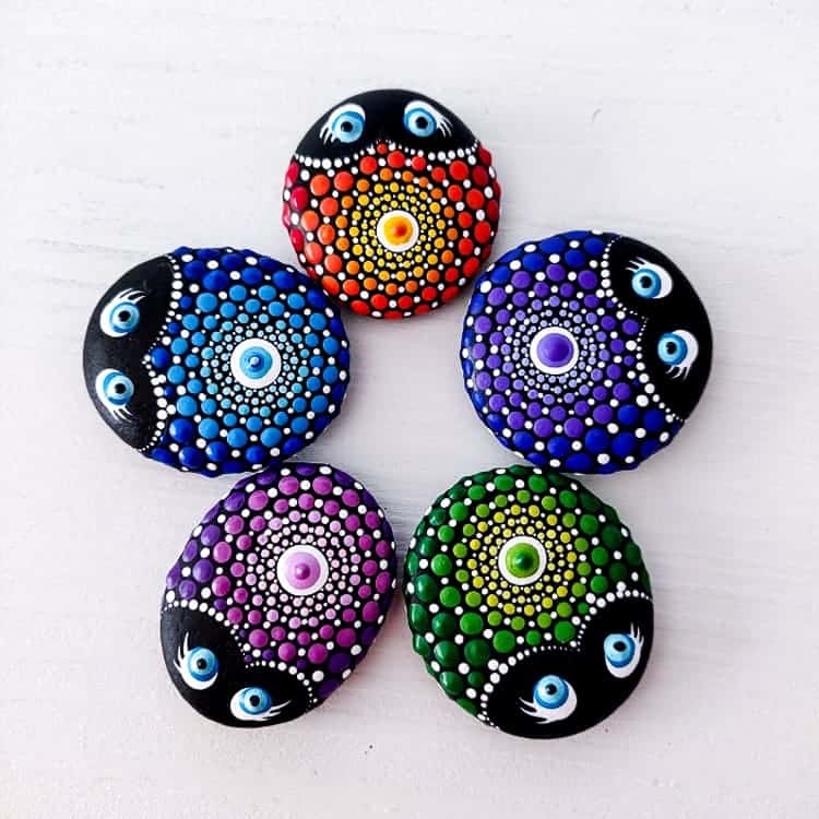 Overhead view of 5 painted rocks with a ladybug mandala design in different colors, placed in a circle.