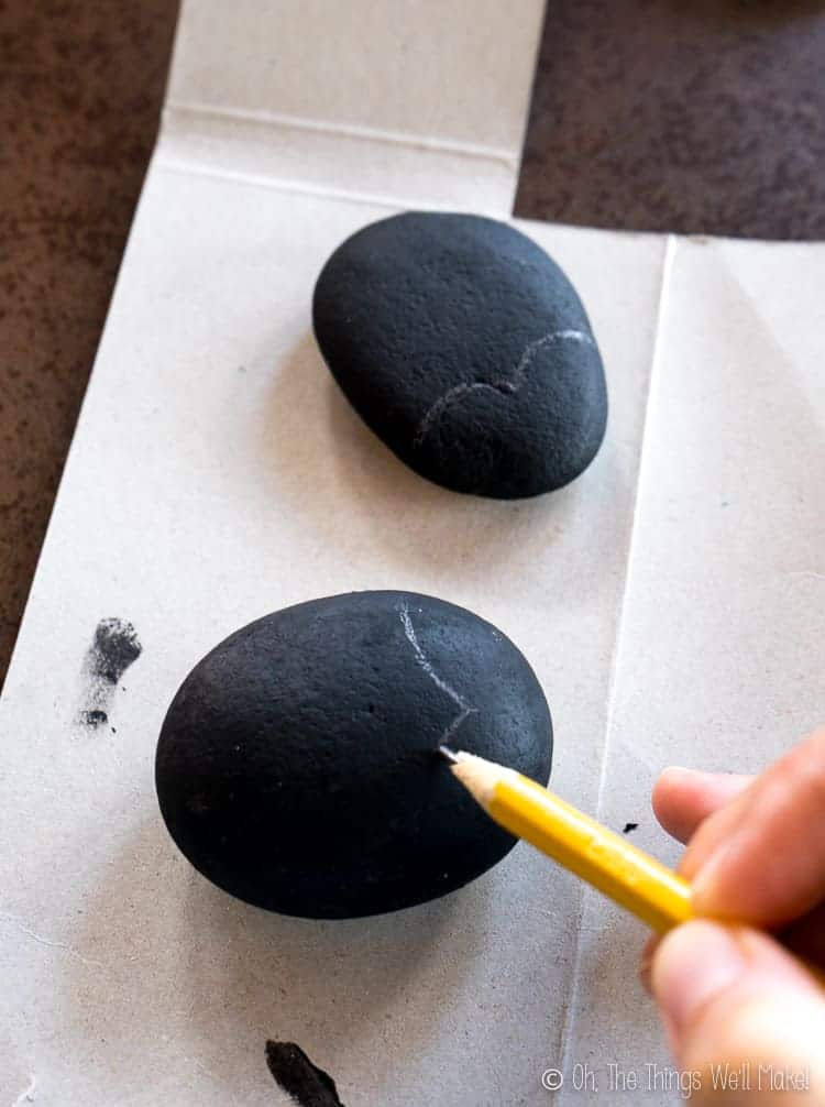 penciling on the design of the ladybug on the black stones.