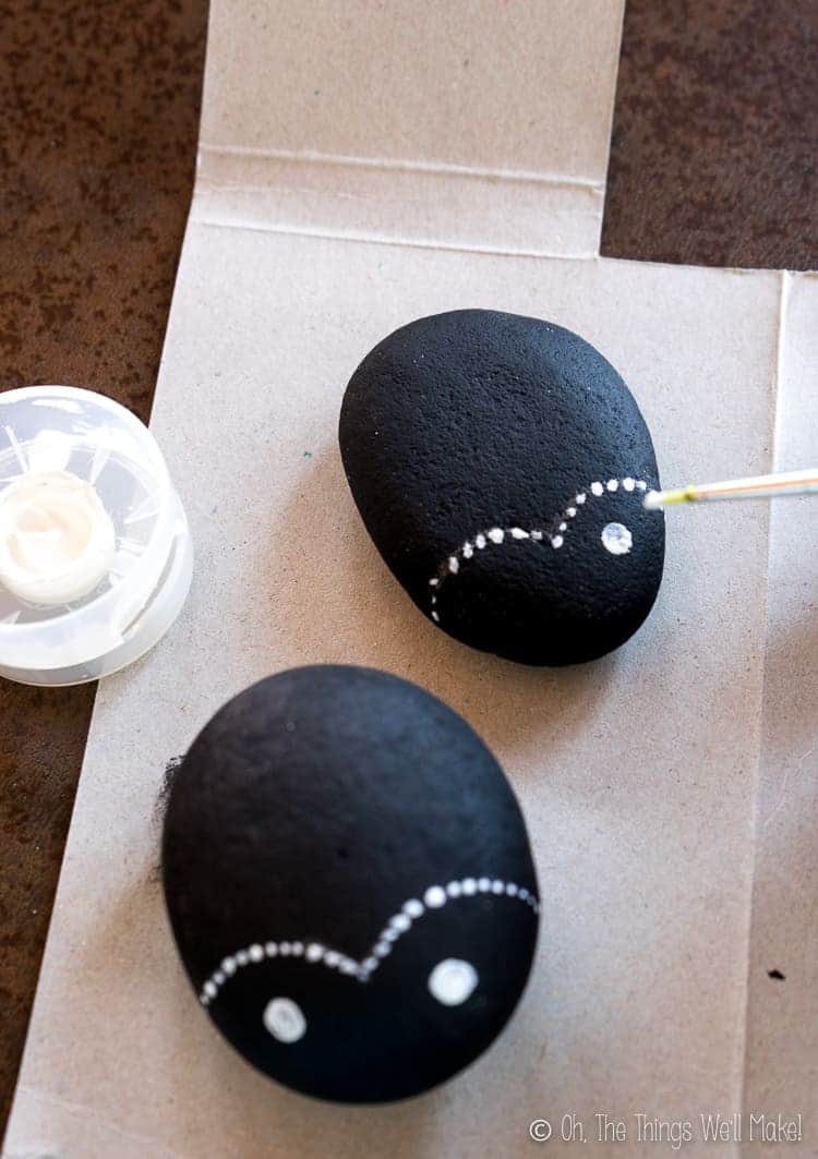 Painting on the white eyes of the ladybug painted rocks.