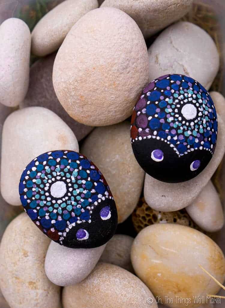 Overhead view of two painted ladybug mandala painted rocks on top of other rounded stones from a rocky beach.