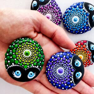 Two ladybug mandala painted stones being displayed on a hand over top of other colorful painted stones.