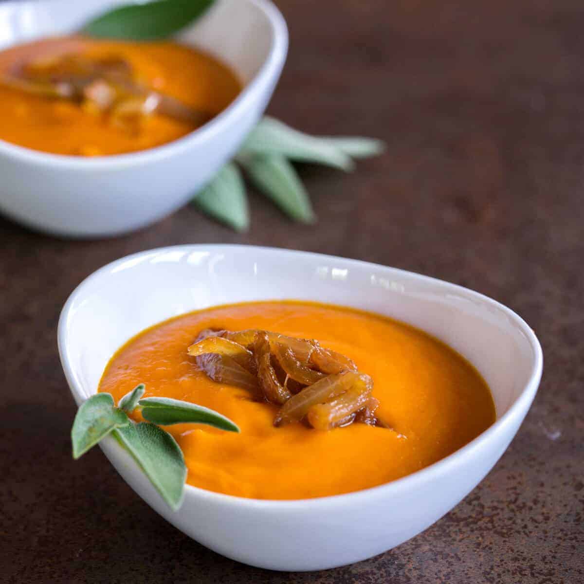 two bowls of a roasted pumpkin soup garnished with fresh sage and caramelized onions.