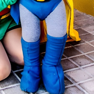 A person wearing a blue and yellow superhero costume with DIY superhero boots standing on a paved surface.