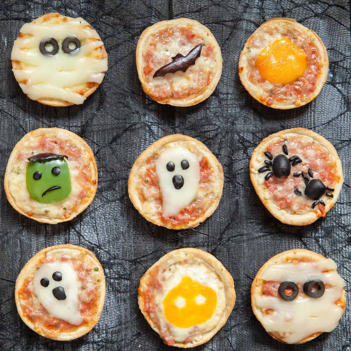 Overhead view of 12 pizzas that have been decorated for Halloween with ghosts, spiders, a bat and other Halloween characters