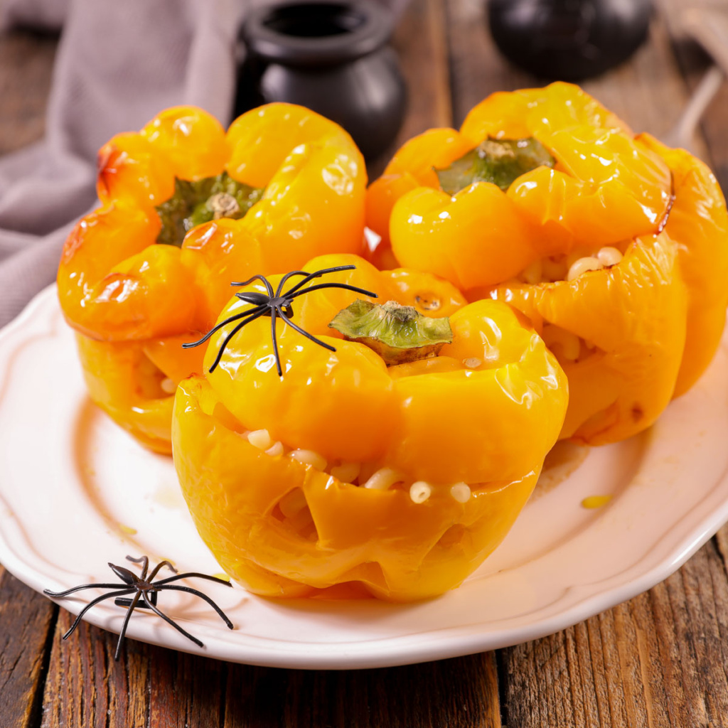 peppers cut into jack-o-lanterns on a plate decorated with plastic spiders