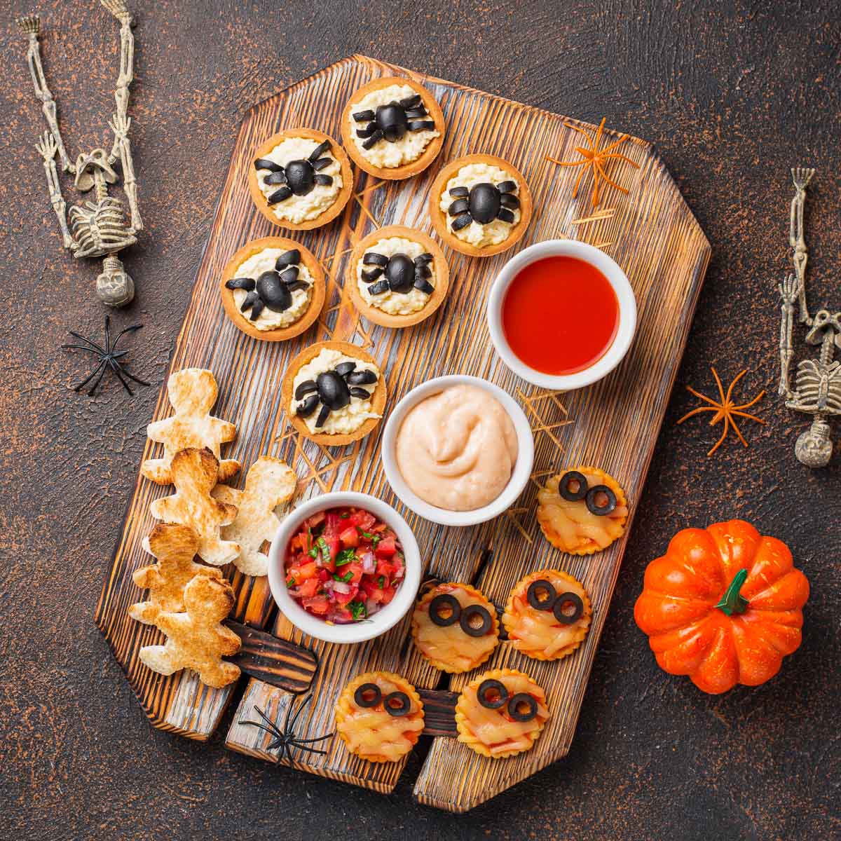 Overhead view of a platter covered with mini mummy pizzas, and tarts covered with olive spiders, amongst other foods.