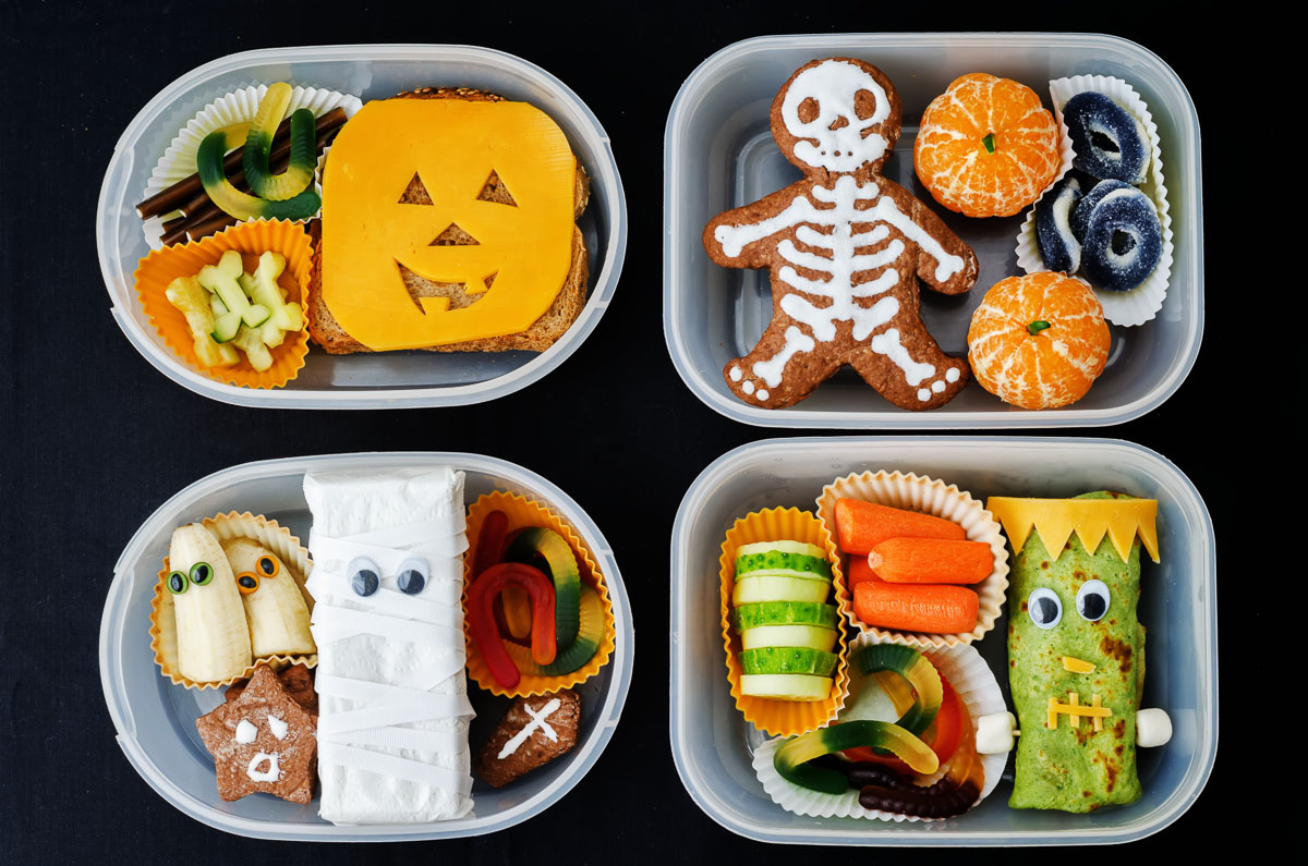 Overhead view of 4 Halloween themed bento boxes with foods decorated with skeletons, monsters, ghosts, pumpkins, and mummies