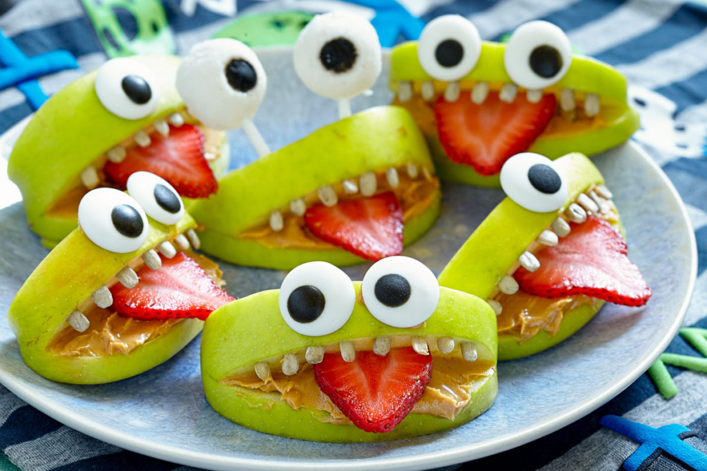6 monsters on a plate made from apple slices, peanut butter and with strawberry slice tongues.