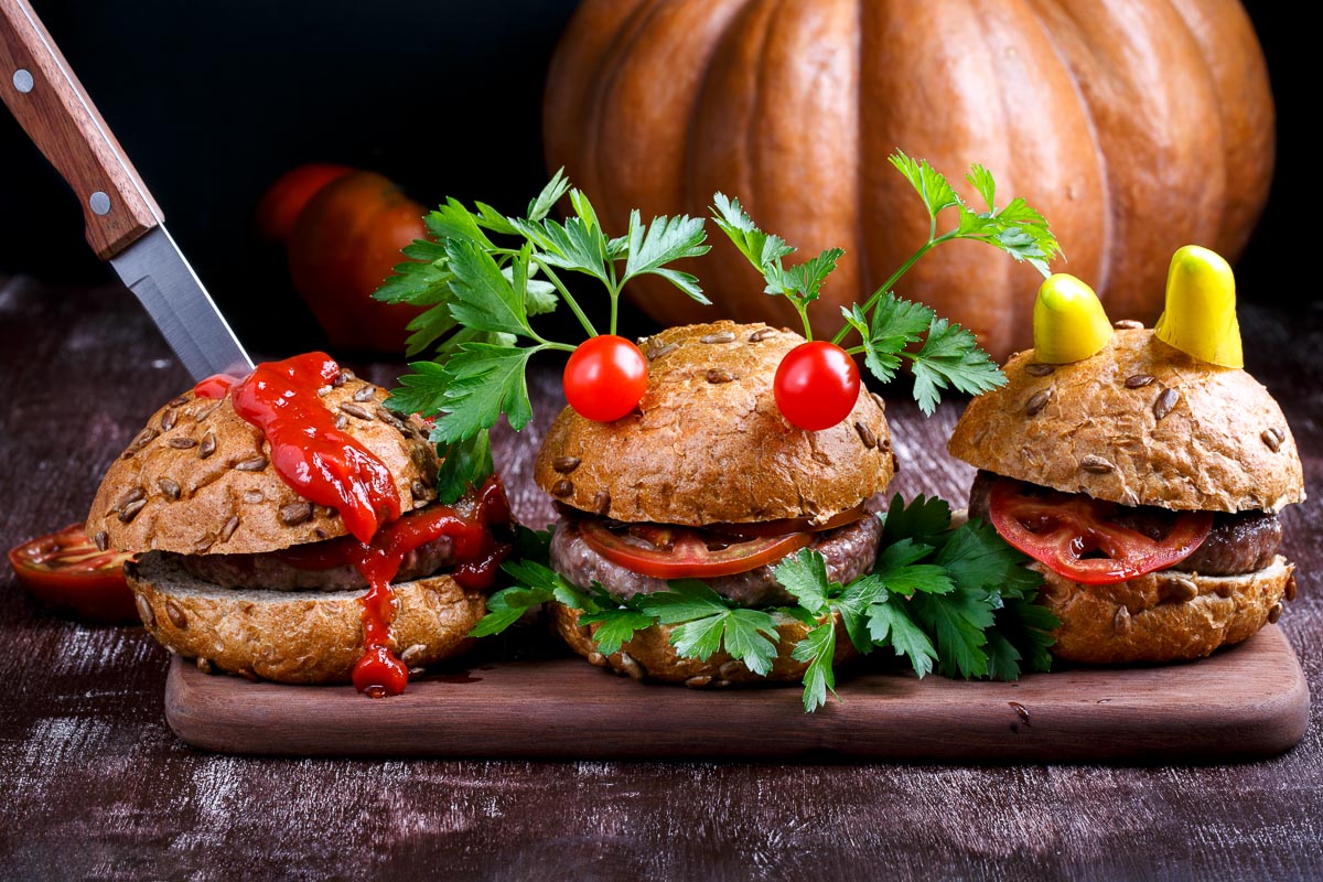 3 hambuergers on a platter. The right two have been made to look like monsters, while the left hamburger has been stabbed with a knife and is oozing ketchup blood.