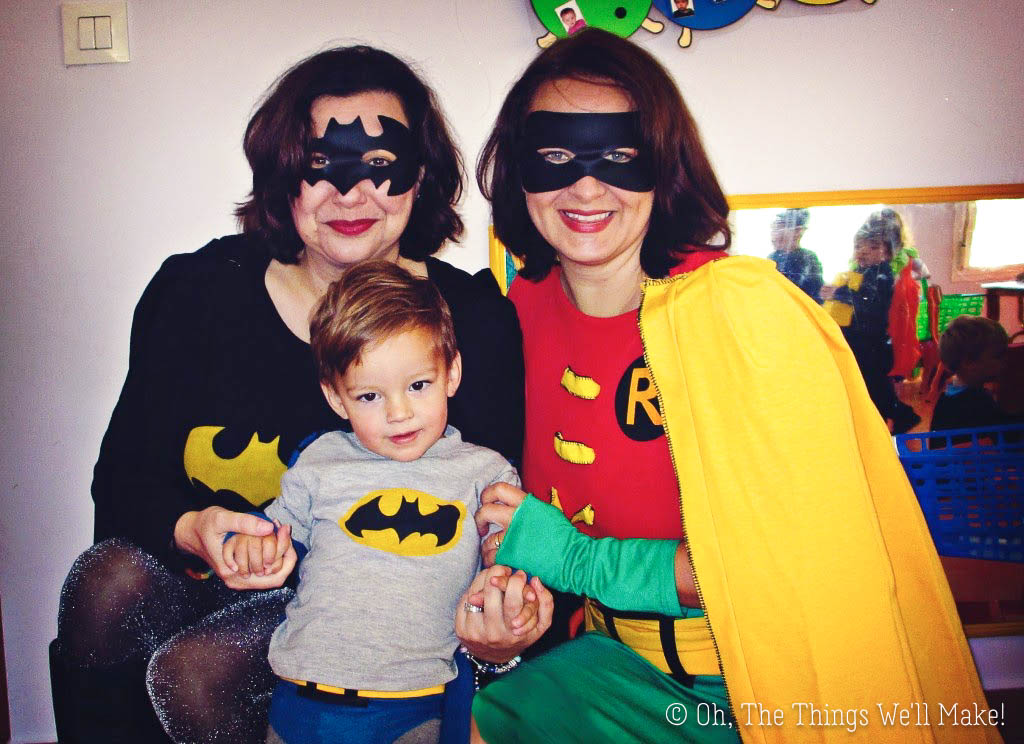 Two women wearing Batman and Robin costumes holding the hands of a young boy wearing a homemade vintage Batman costume.