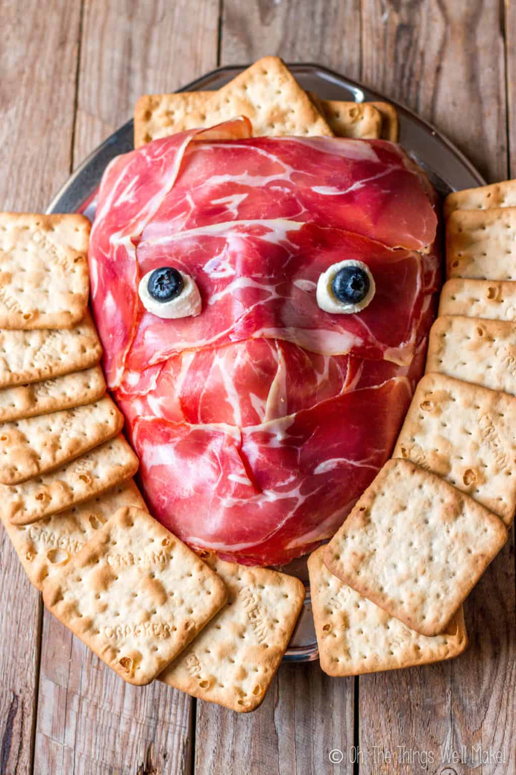 Overhead view of a prosciutto face on a platter, surrounded by crackers.