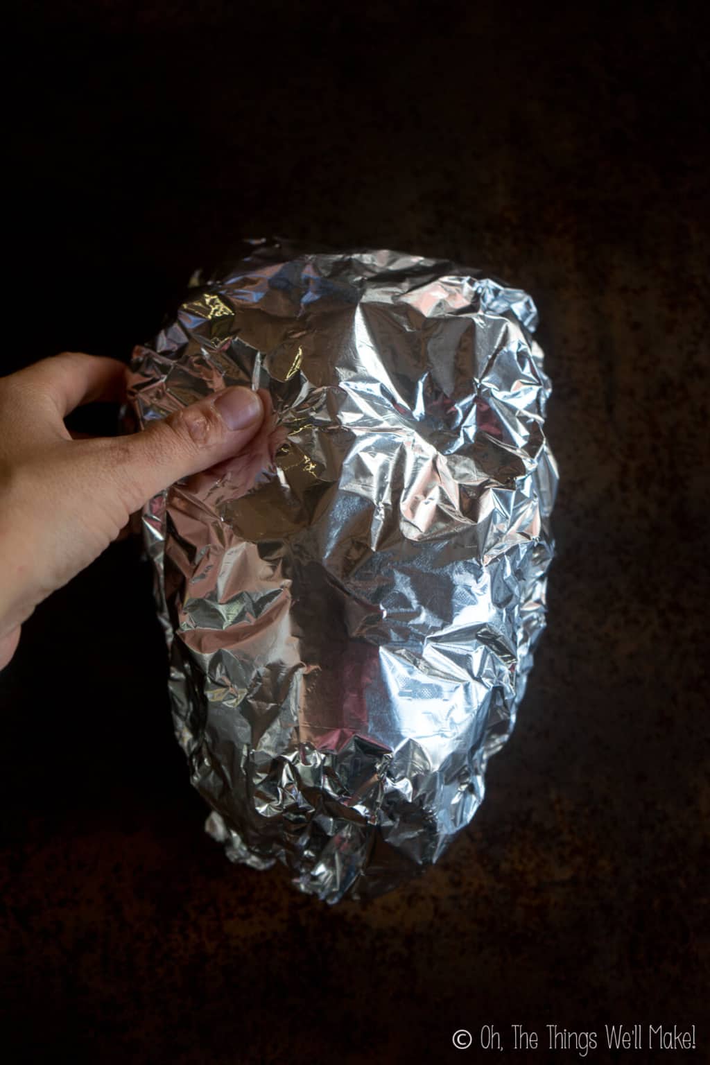 A thumb pressing into an oval spheroid covered with aluminum foil to make eye socket shapes.