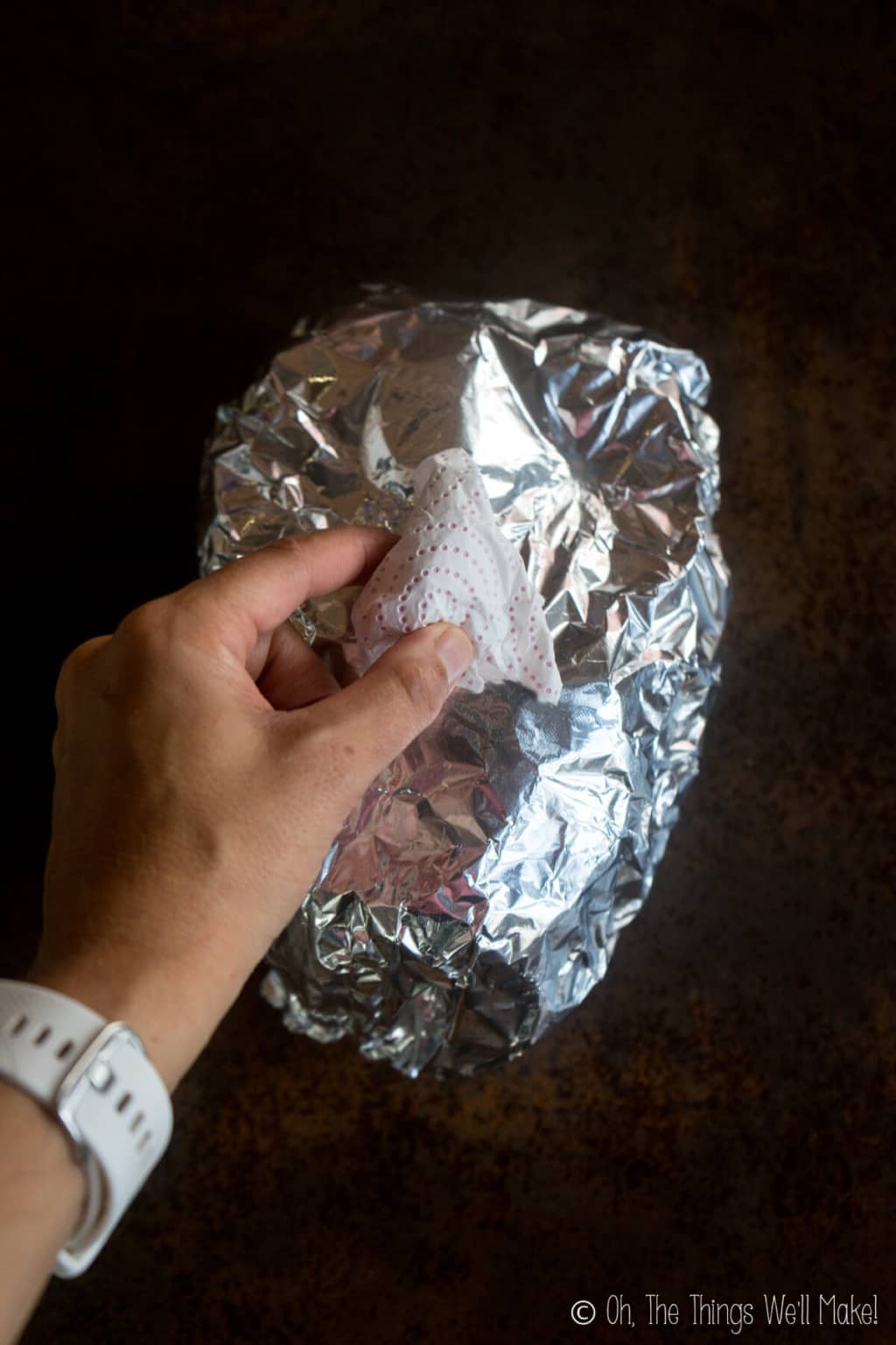 A hand pressing white tissue paper into a shape of a nose into an oval spheroid covered in aluminum foil.