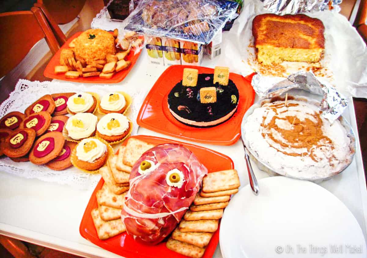 Table with Halloween foods including a prosciuttos face and a pumpkin shaped cheeseball with crackers.