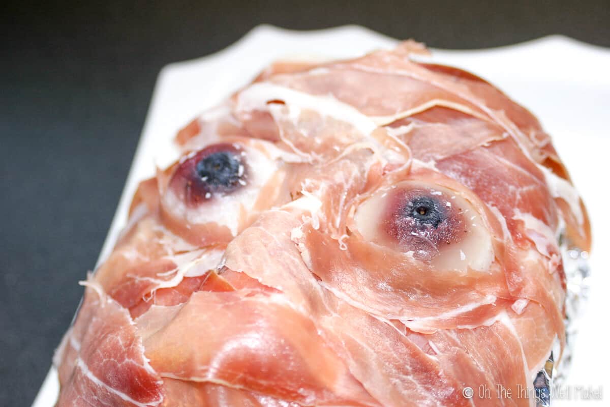 Close up of a prosciutto ham face showing the gummy gelatin eyeballs with blueberries as pupils.