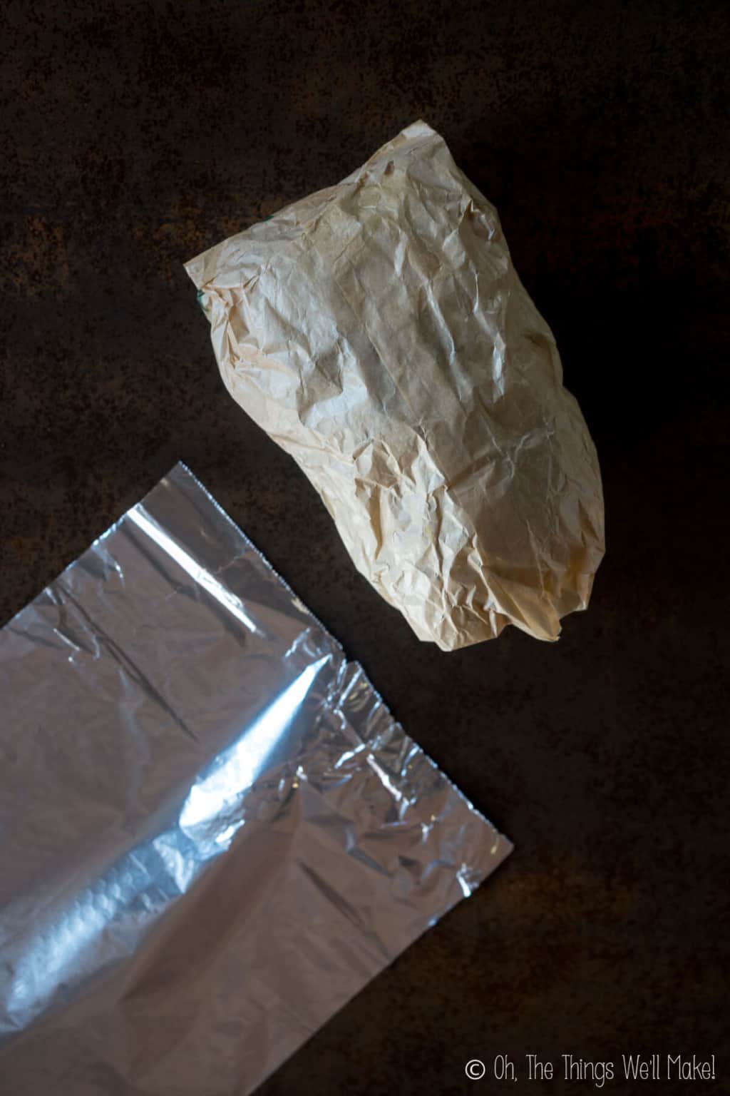 A brown paper bag filled with paper scraps next to a sheet of aluminum foil.