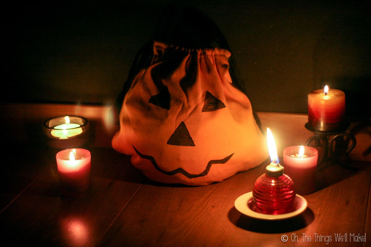 A jack-o'-lantern trick-or-treat bag surrounded by lit candles and a small oil lamp.