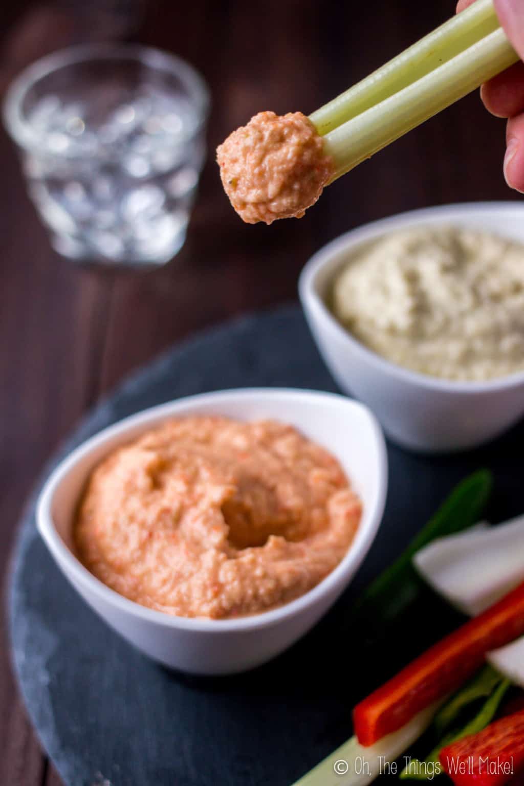 Close up of celery stick top with roasted red pepper zucchini hummus on top of a bowl filled with the same hummus.
