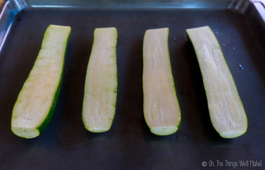 Zucchini sliced in half lengthwise on a baking tray