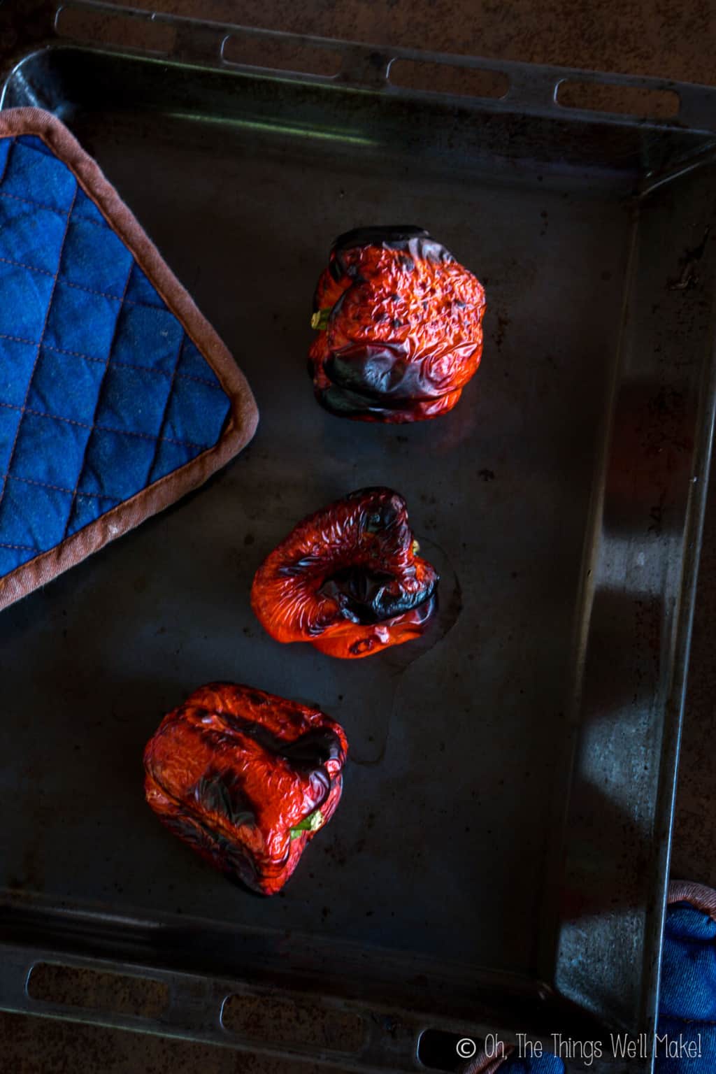 Top view of three roasted red peppers with char-broiled skin on a baking pan