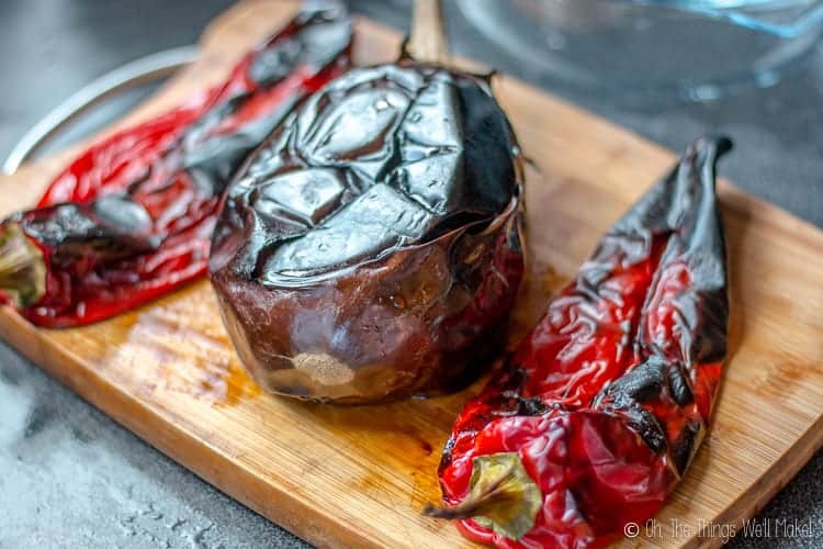 Charbroiled red Italian peppers with a charbroiled eggplant on a bamboo cutting board.