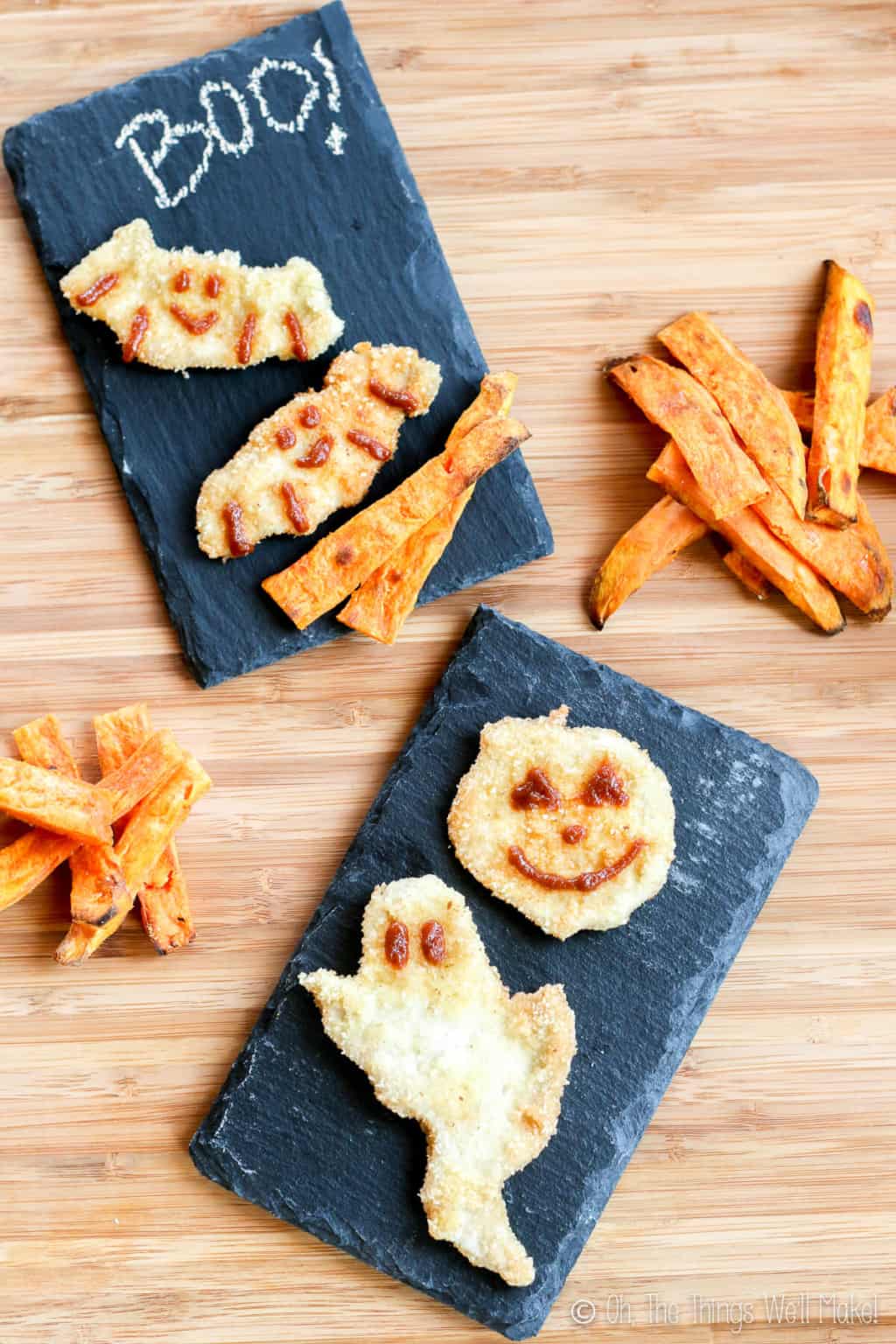 Halloween chicken nuggets placed on black rectangular plates, shaped like ghosts, pumpkins, and bats, and decorated with BBQ sauce. There are several pieces of sweet potato fries around the plates.