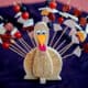 A Thanksgiving centerpiece shaped like a turkey that holds appetizer skewers.