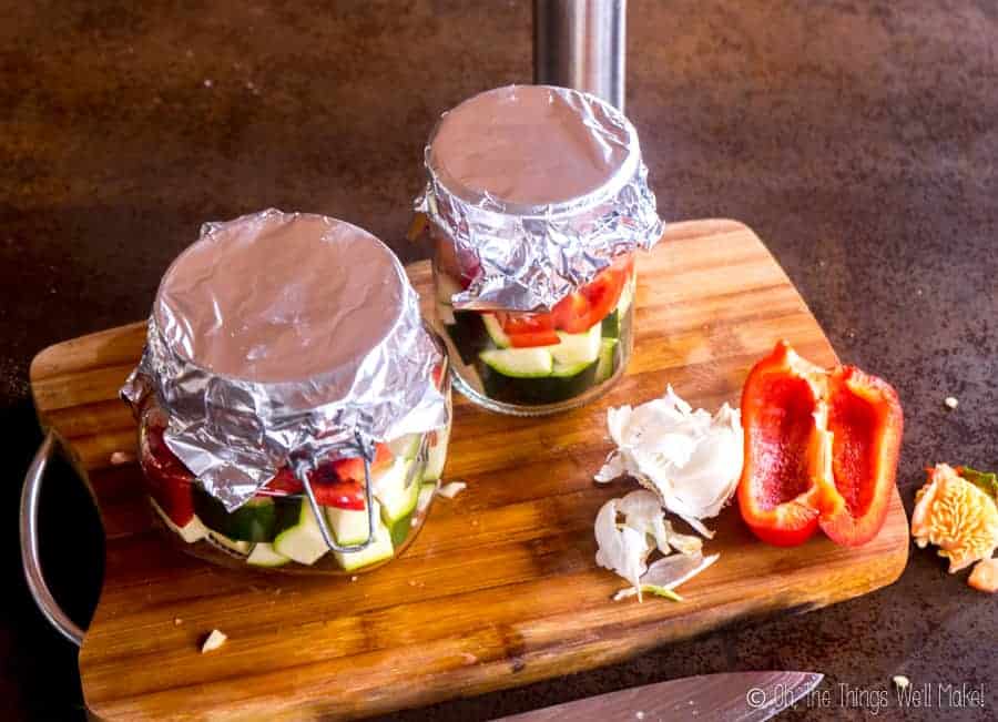 Jars filled with vegetables and salmon, covered with foil.