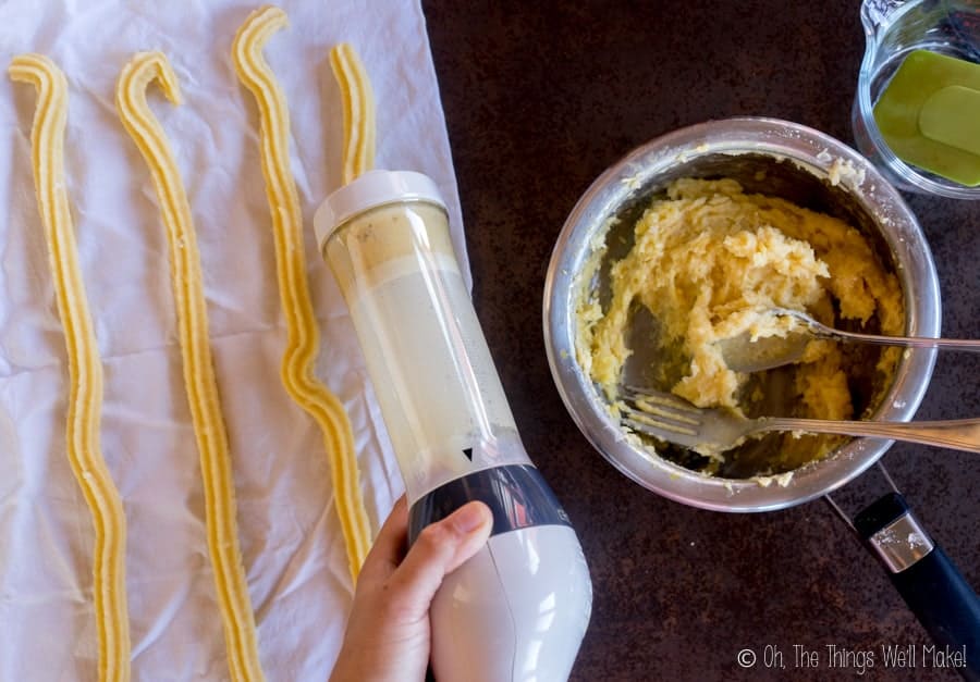using a cookie press to dispense churros onto a clean, white cloth.