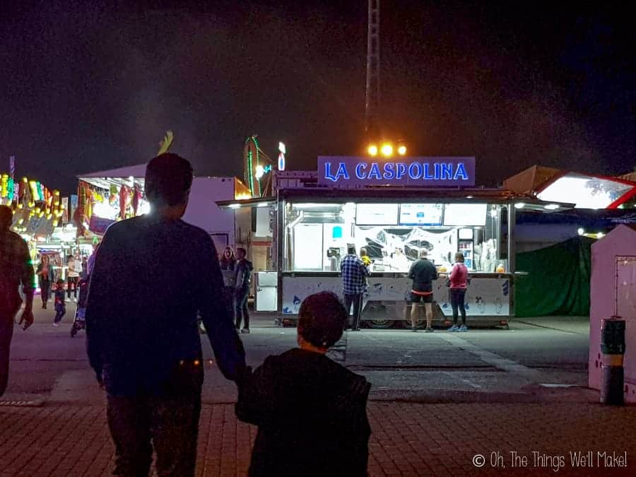 A boy with his father walking towards the Caspolina churros truck at a Spanish fair.