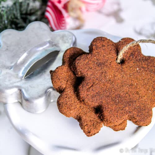 Two homemade cinnamon applesauce ornaments on a stand with the cookie cutter used to form them