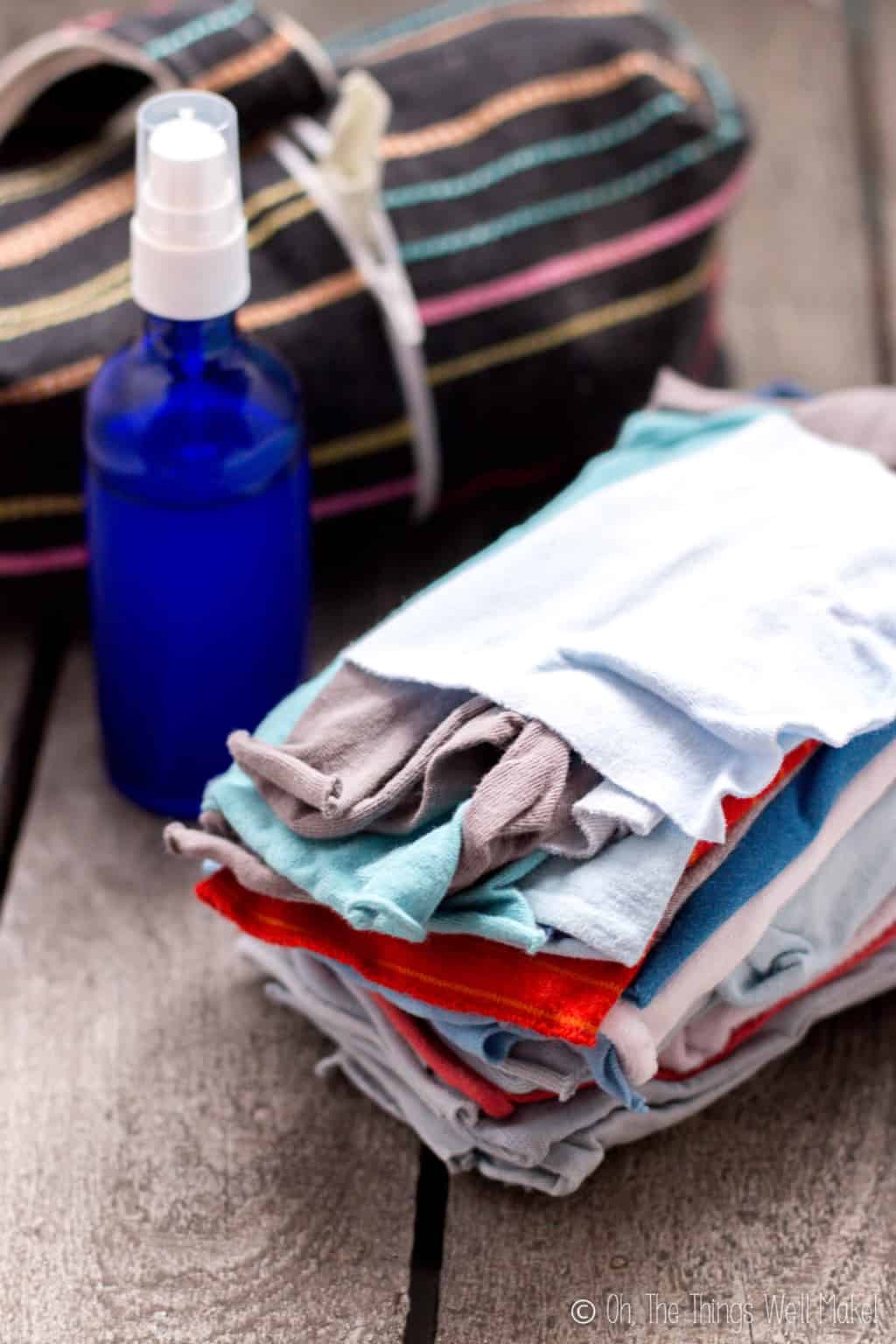 A stack of colorful homemade cloth wipes in front of a blue glass bottle filled with wipe solution.