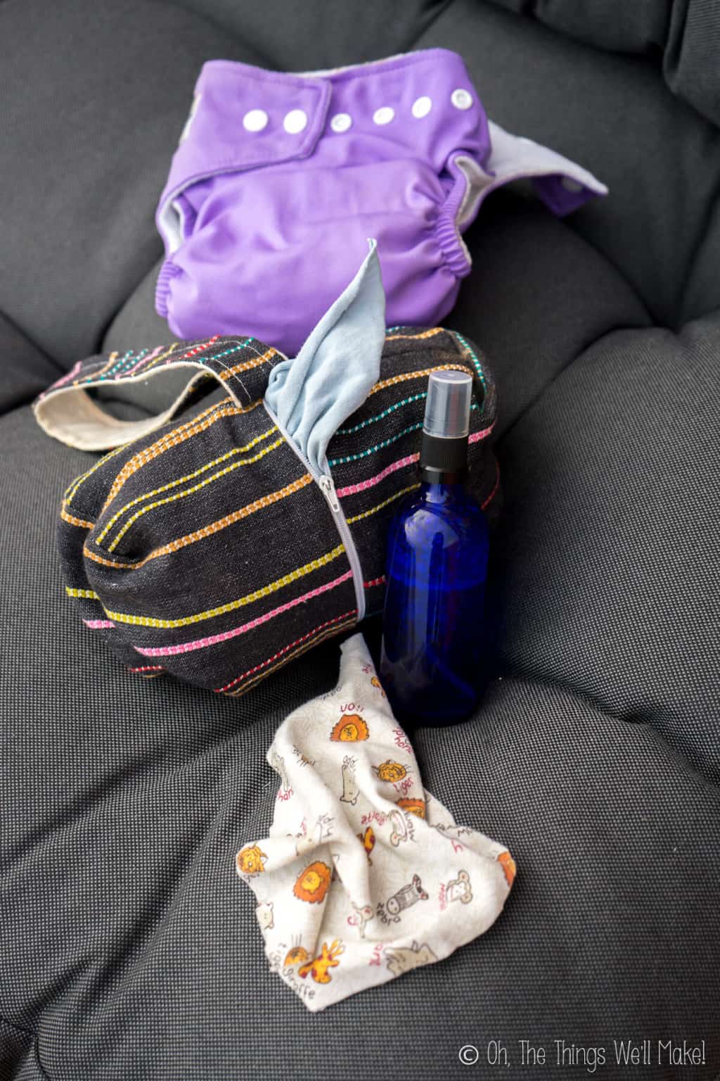 A small blue glass bottle with baby wipe solution, a black with stripes design cloth wipes dispenser, and a purple cloth diaper.