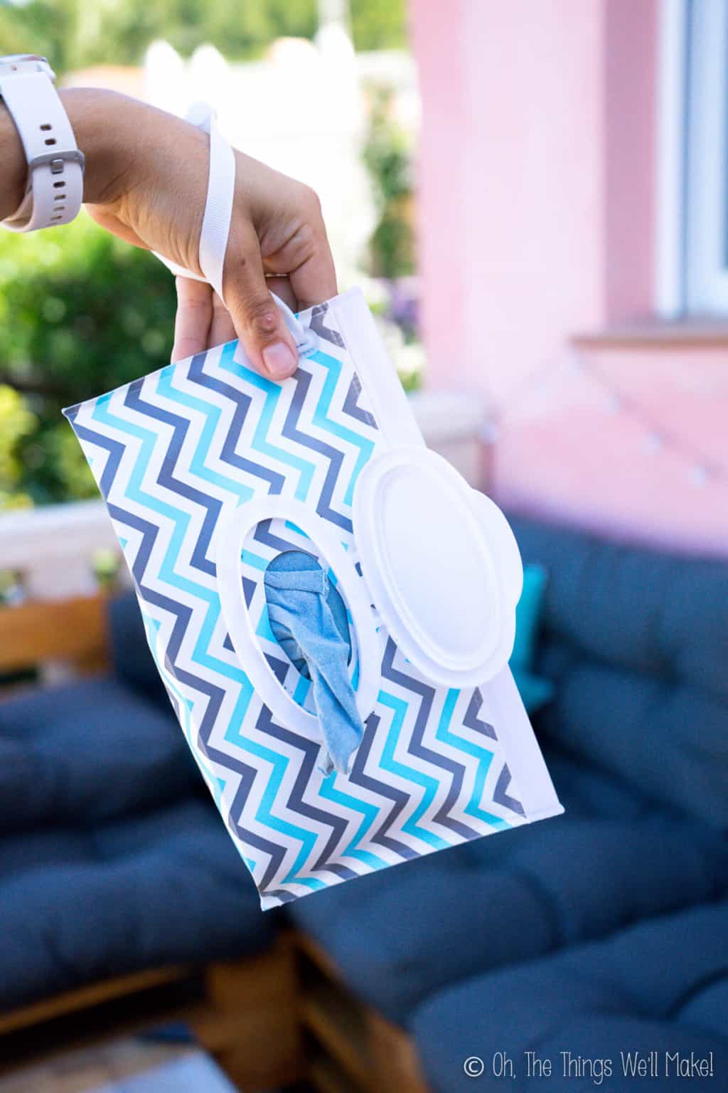 A hand holding onto a chevron printed plastic pouch wipes dispenser open with a cloth wipe peaking out.