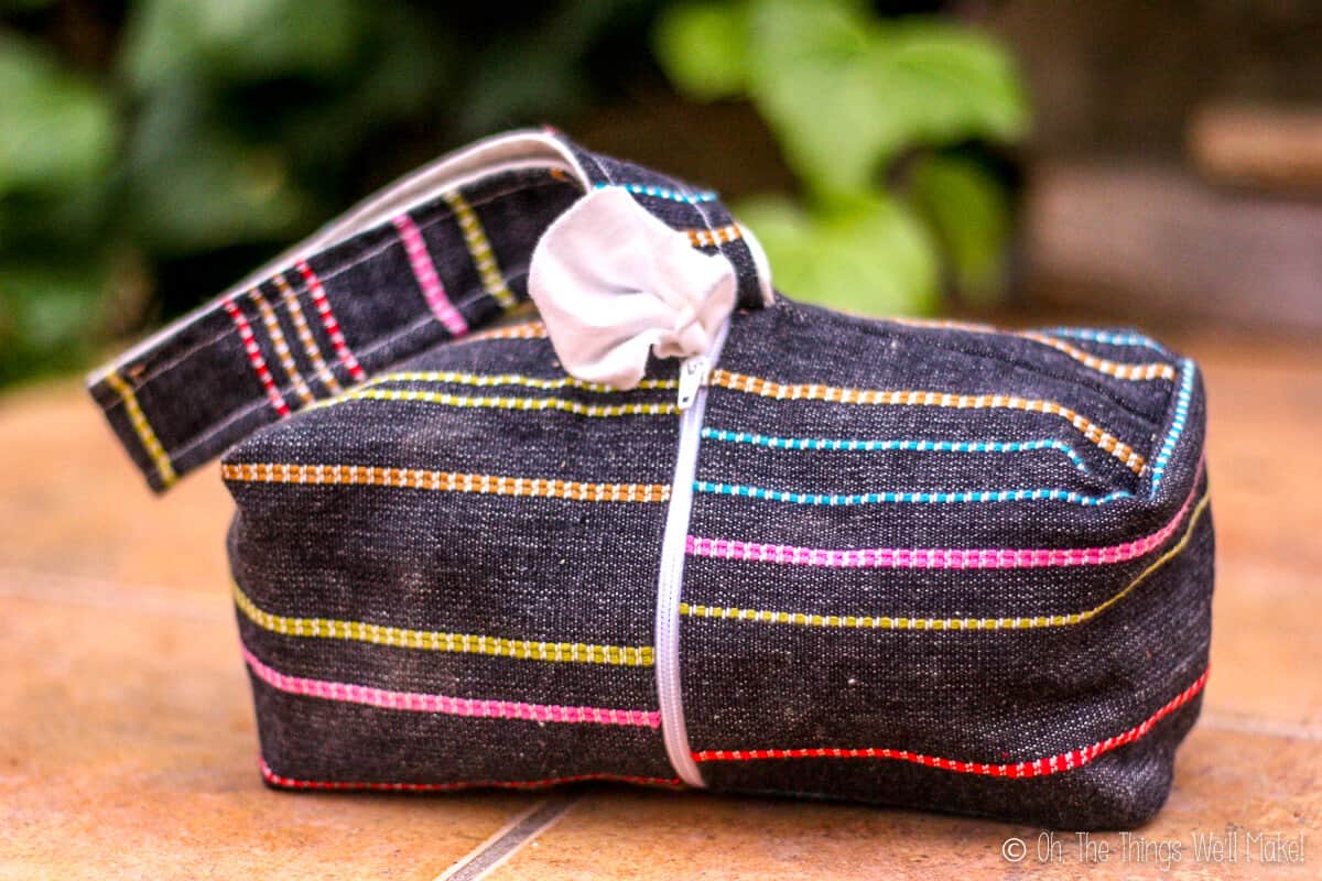 A rectangular black with colorful stripes fabric bag that is actually a baby cloth wipes dispenser.