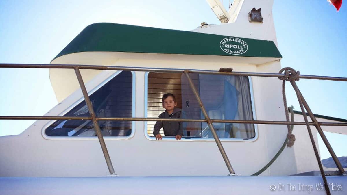 A young boy looking out the window of a white fishing boat.