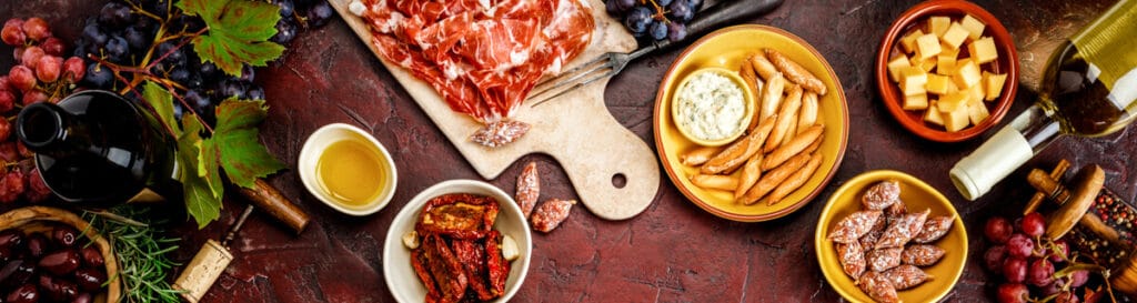 A tablescape with wine, sliced ham and dried sausgaes, crackers, and cheese.