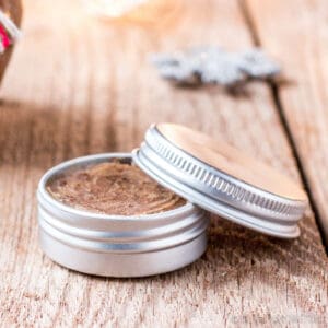 Closeup of an aluminum tin filled with a brown sugar lip scrub. The lid of the tin is resting over the side of the tin.