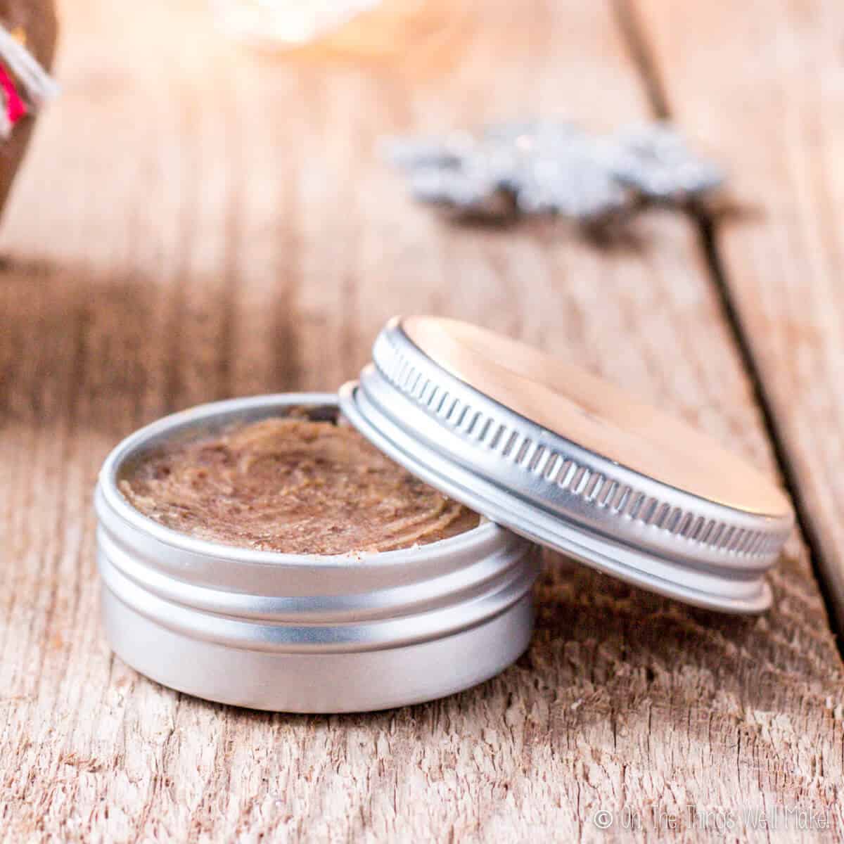 Closeup of an aluminum tin filled with a brown sugar lip scrub. The lid of the tin is resting over the side of the tin. 