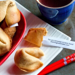 Overhead view of several homemade fortune cookies. One has been opened to show a fortune that reads "You are fortunate to have found thethingswellmake.com".