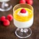 Overhead view of a glass of homemade panna cotta in front of another one, both garnished with mango puree and raspberries.