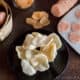 Homemade prawn crackers on a plate in front of uncooked homemade prawn crackers and a roll of prawn crackers dough.