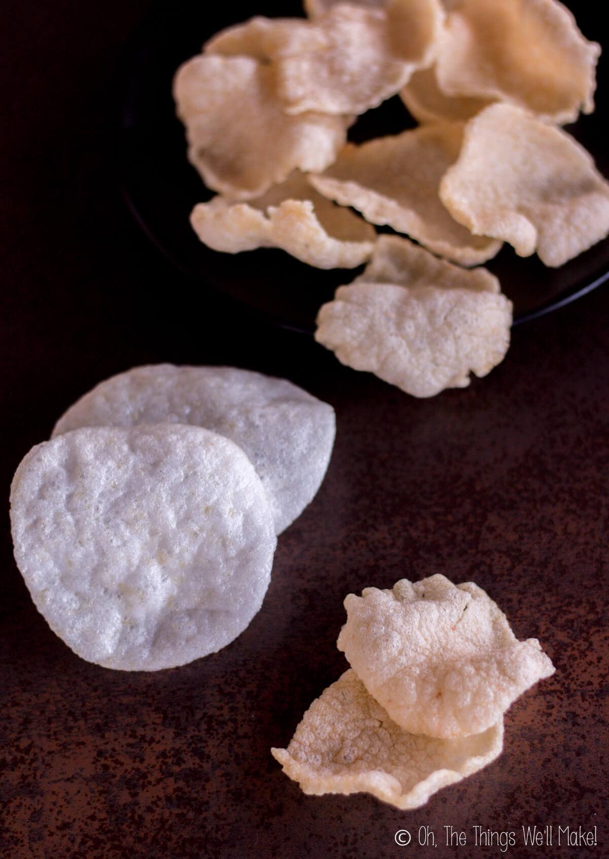 Two homemade prawn crackers in front of 2 store-bought ones. A plate of homemade prawn crackers can be seen in the background.