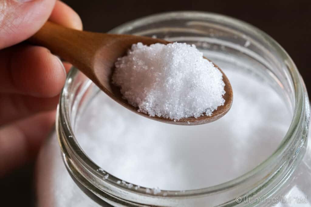 Overhead view of xylitol on a wooden spoon over a jar of it.