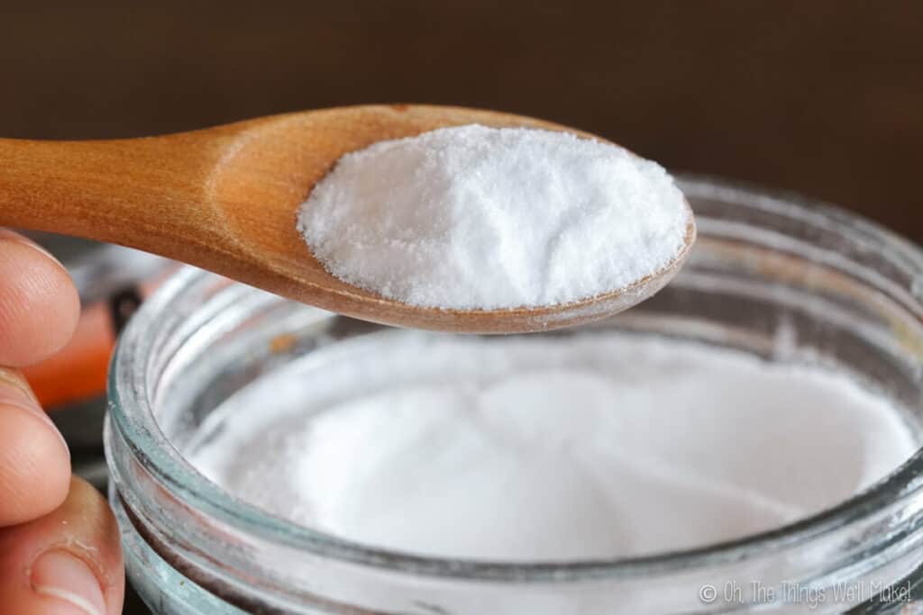 A wooden spoon full of baking soda held over a glass jar filled with baking soda.