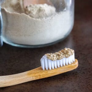 Closeup of tooth powder on a bamboo toothbrush. In the background theres a glass jar filled with the homemade tooth powder.
