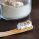 Closeup of tooth powder on a bamboo toothbrush. In the background theres a glass jar filled with the homemade tooth powder.