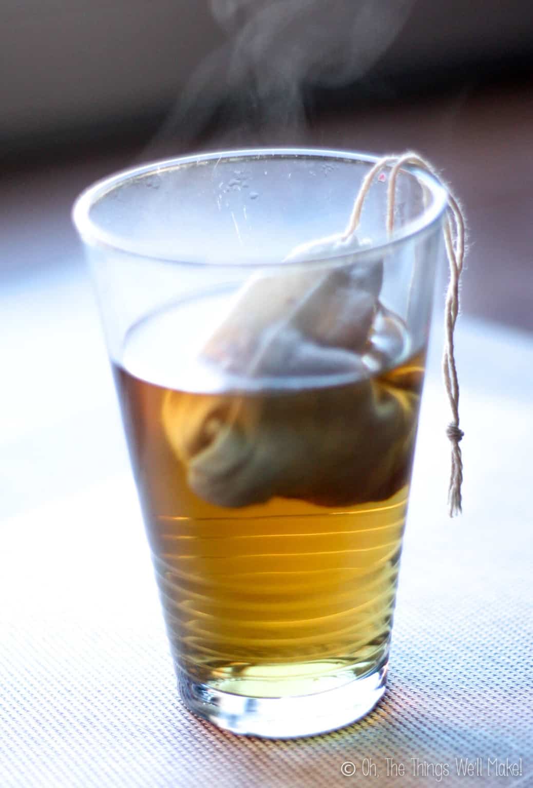 A close up of a glass with steeping a tea bag filled with rose petals.